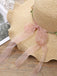 Beige straw hat with a sheer pink ribbon on a wooden surface