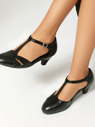 Black leather shoes with T-straps worn by a person on a white background