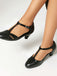 Black leather shoes with T-straps worn by a person on a white background