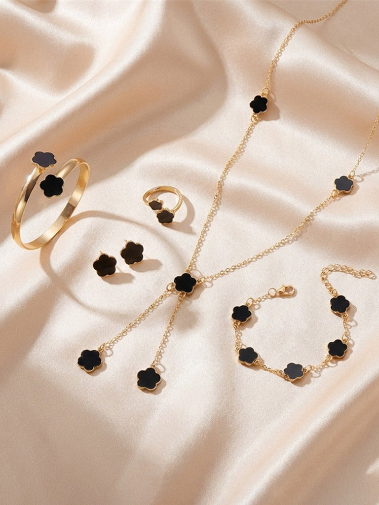 Gold jewelry set with black flower-shaped stones on a beige fabric background