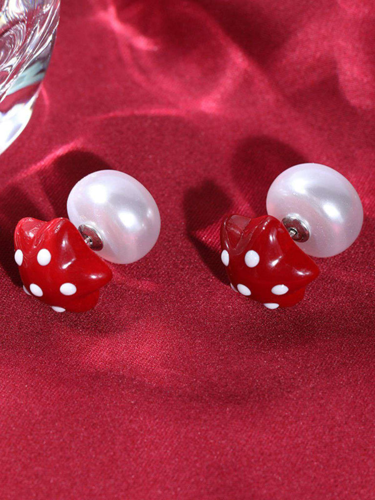 Pair of earrings with red dice and pearl-like stones on a red fabric background