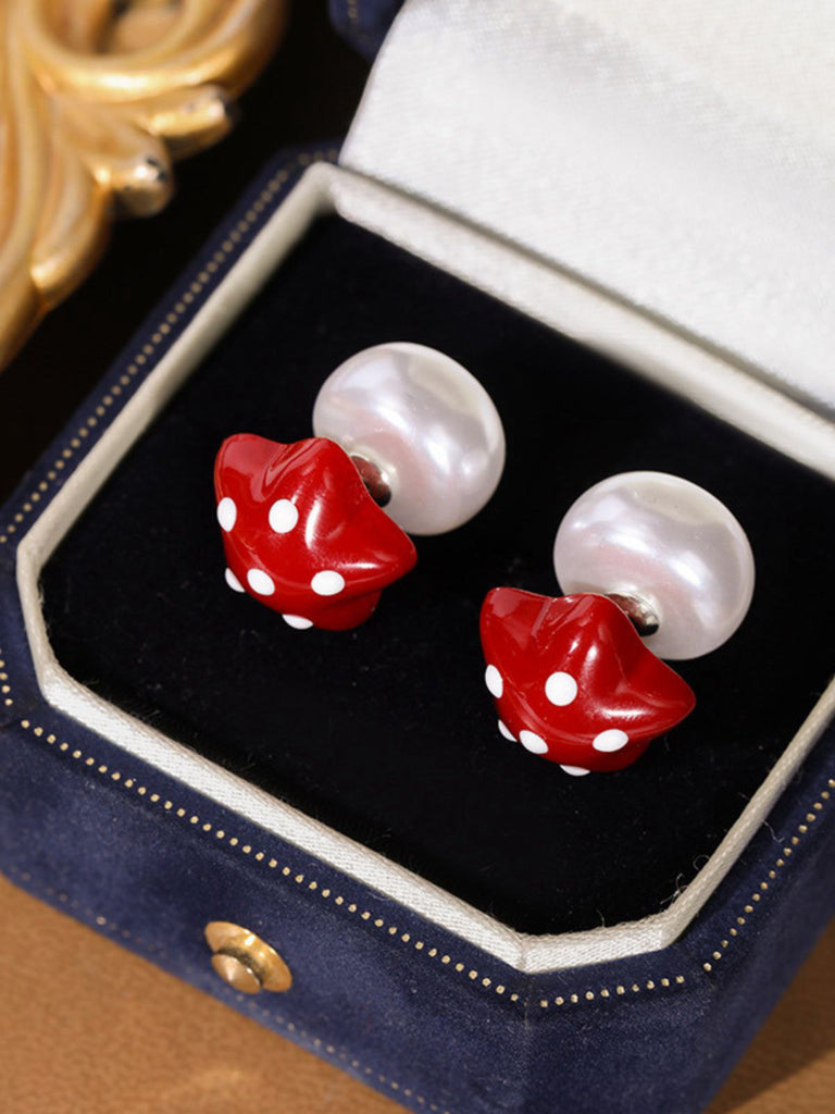 Pair of earrings with red mushroom design and pearl-like elements in a jewelry box.