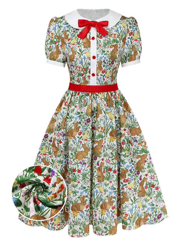 Une robe trapèze à manches courtes d'inspiration vintage, ornée d'un imprimé fantaisiste de lapins et de fleurs sauvages, d'un col Claudine blanc et d'un nœud rouge décoratif.