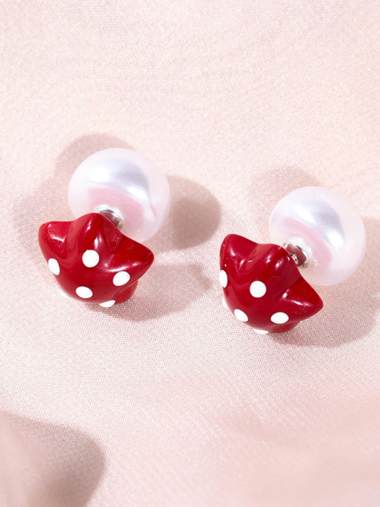 Pair of earrings with red mushroom-shaped studs on a light pink background