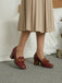 Red shoes with brown bow details worn by a person in a beige skirt.
