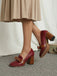 Red high-heeled shoes with brown soles worn by a person in a beige skirt.
